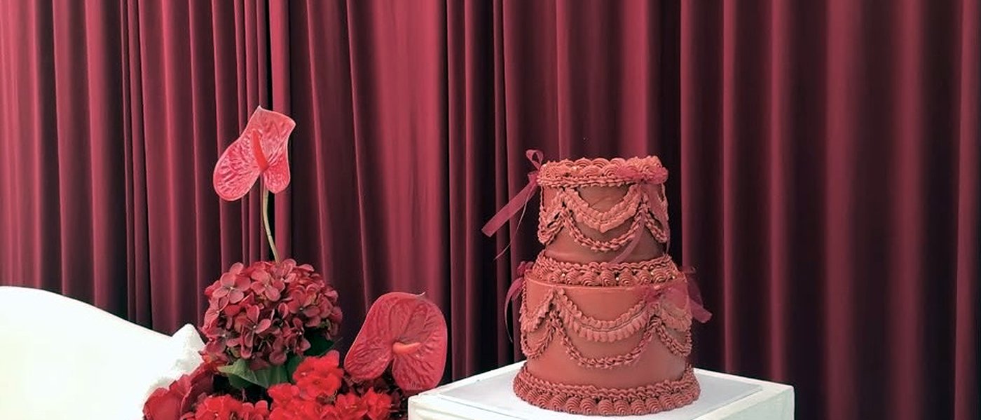 Deep red vintage cake on a plinth beside red florals at an event