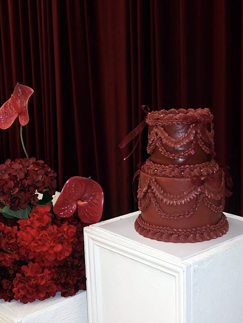 Deep red two-tier vintage cake with piped garlands and ribbon bows